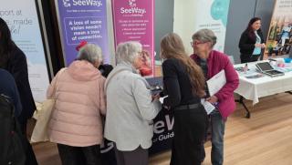 SeeWay team member Kaye talking with Clients at a community event, all with their backs to the camera as they look the SeeWay display table and banners.