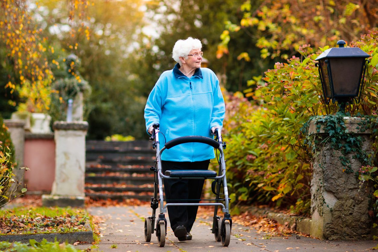 Older person walking in park using a mobility walker