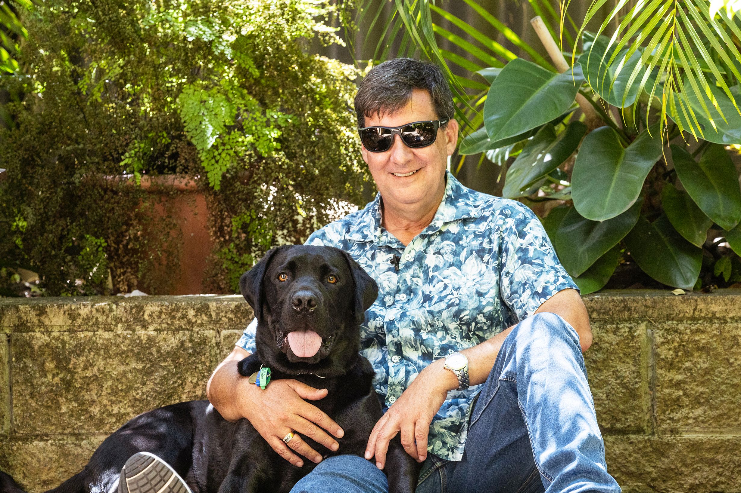 Jason and his black Labrador Guide Dog Tyson sit outside posing for a photo.