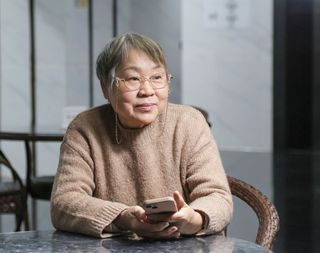 Seated older woman holding her smartphone and looking into the distance.