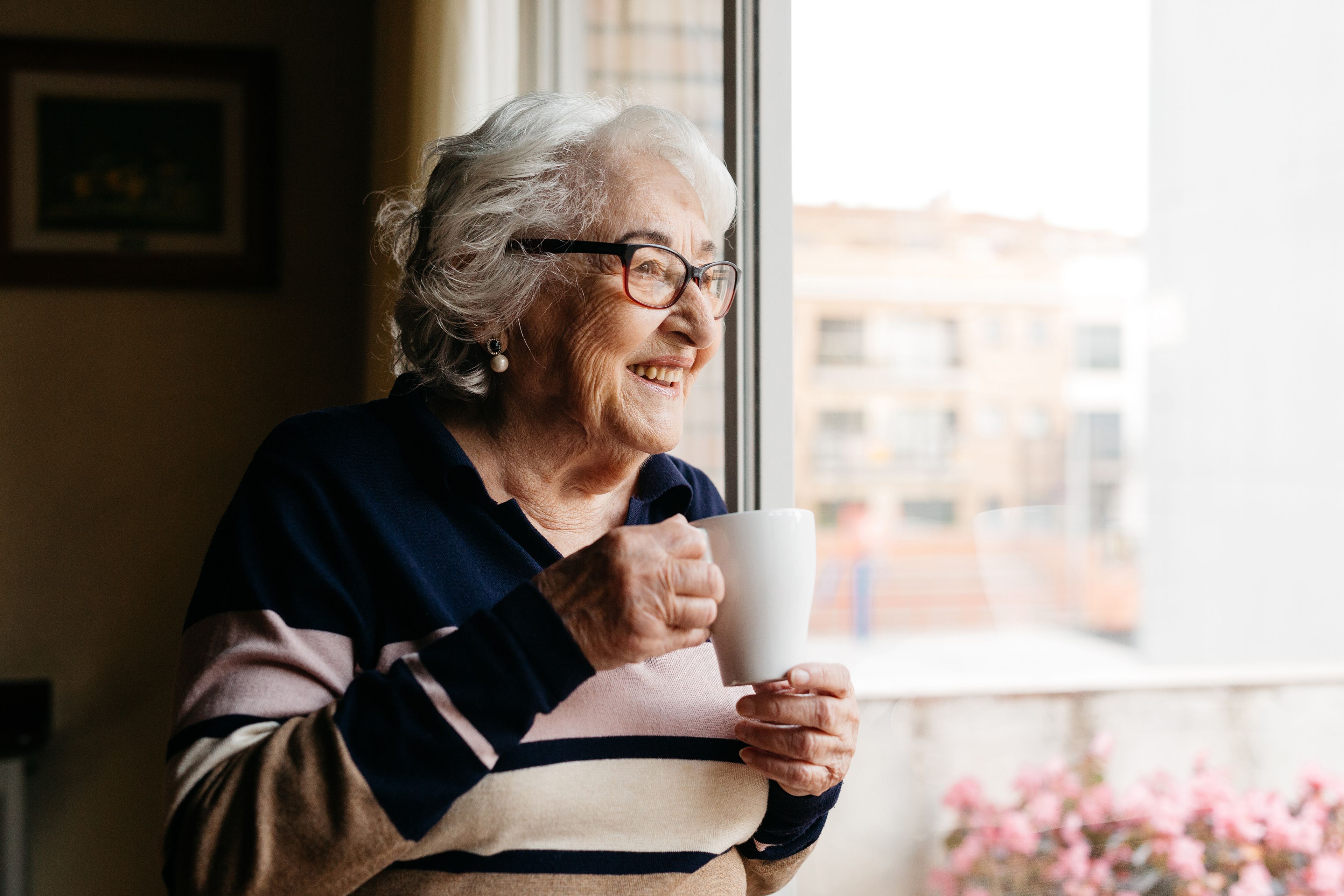 Smiling older person drinking tea while looking out window