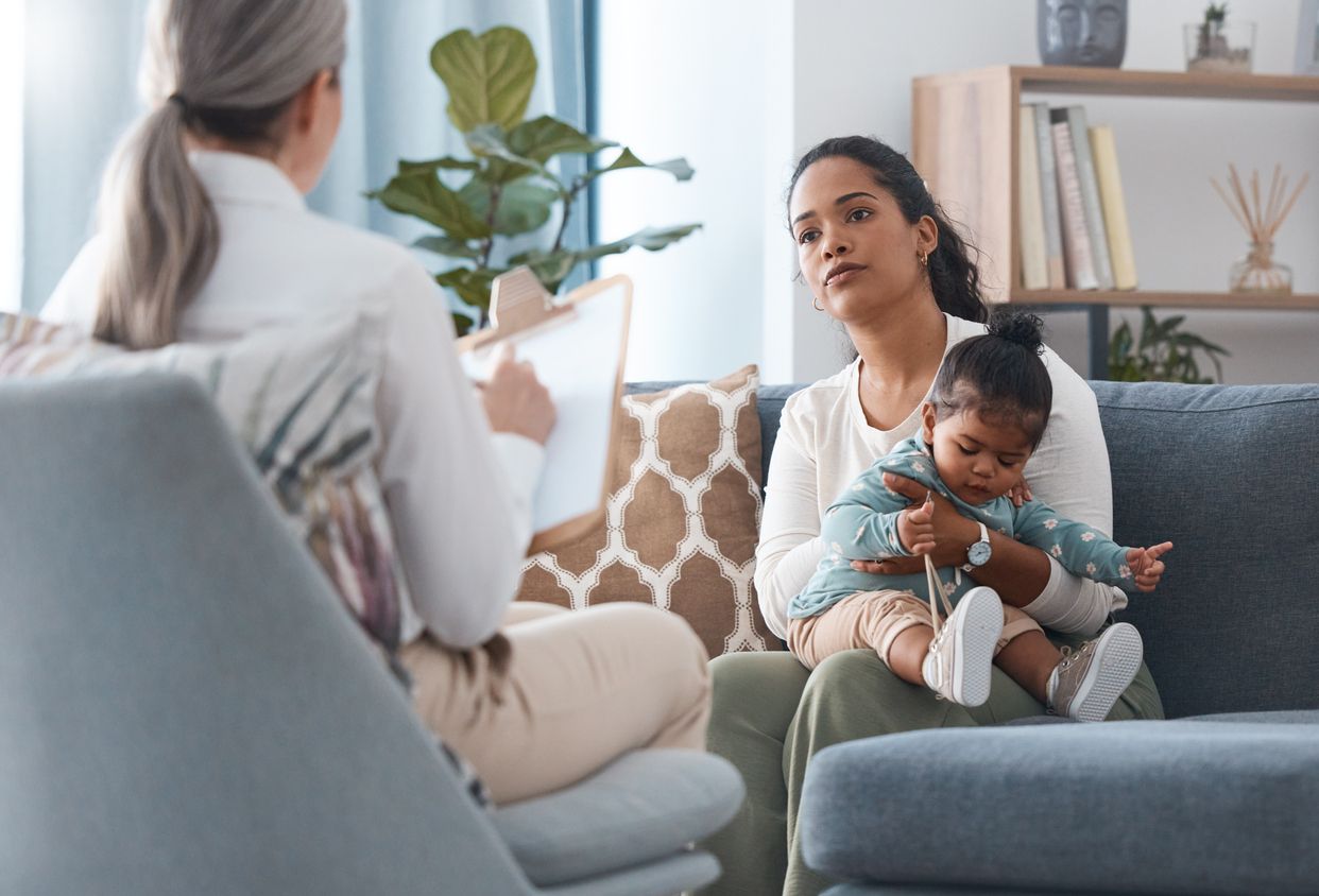 Mother and toddler seated on a couch, in discussion with a medical professional