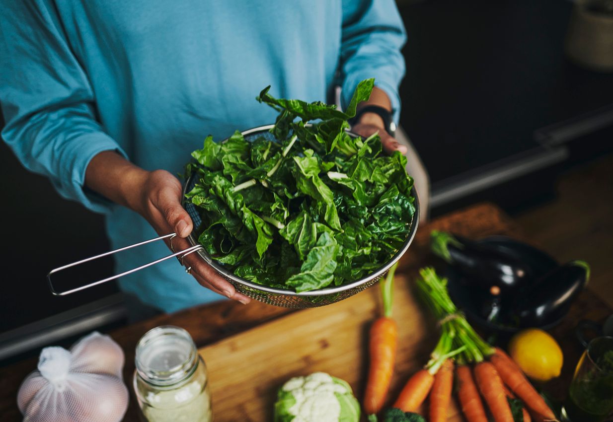 A person holding a strainer filled with assorted leafy green vegetables.
