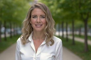 A smiling woman stands facing the camera in a park