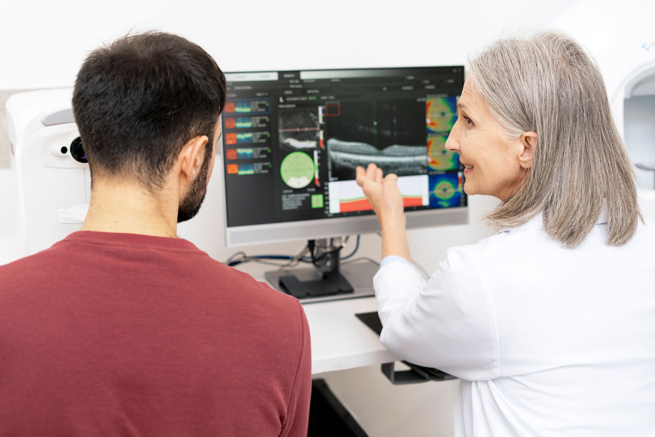 An eye care professional shows her patient the results of his OCT scan on a computer.