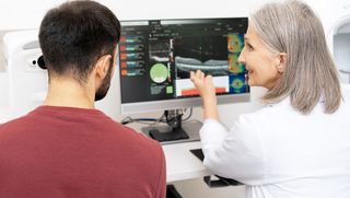 An eye care professional shows her patient the results of his OCT scan on a computer.