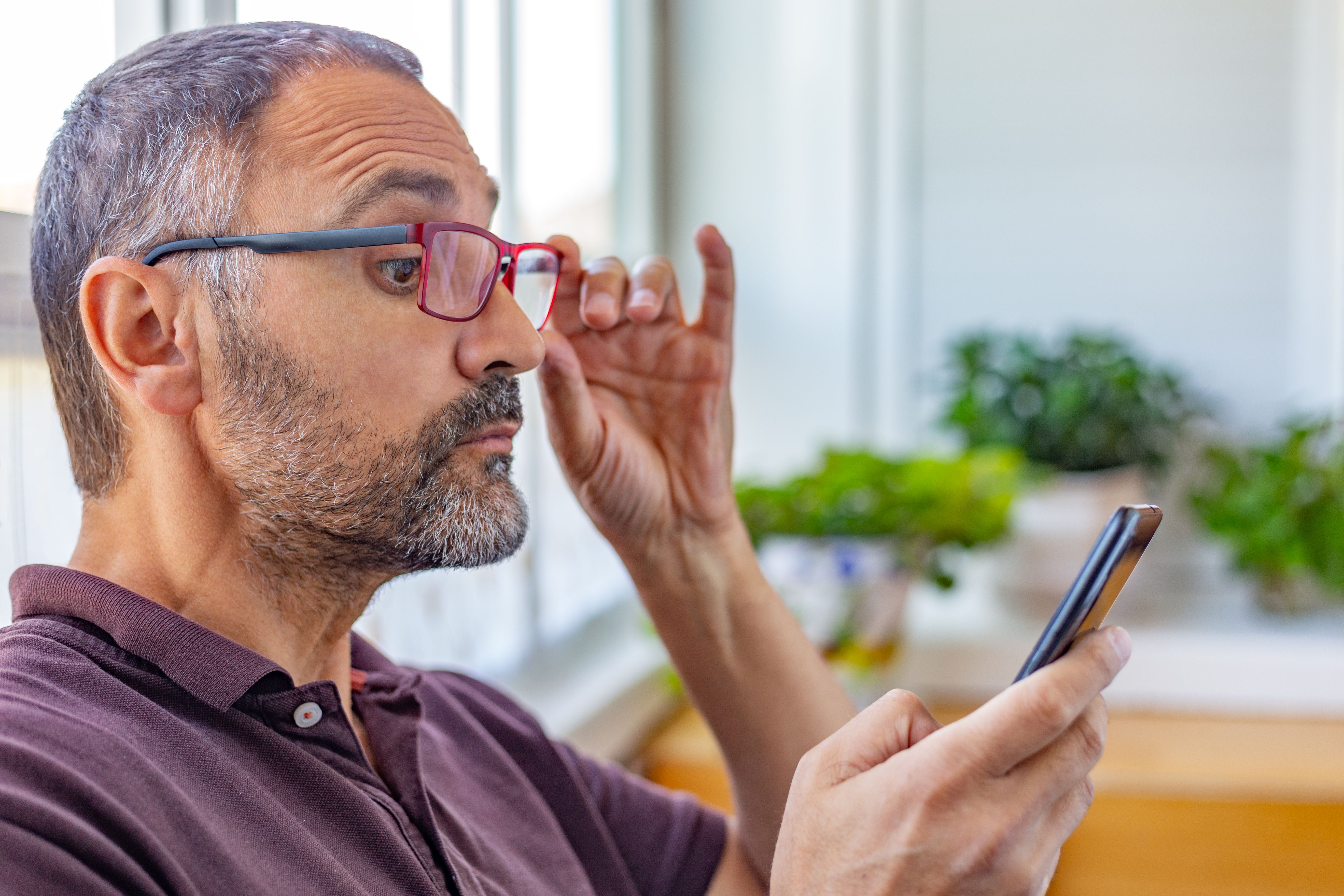 Person shifting glasses to view mobile phone