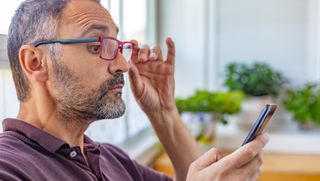 Person shifting glasses to view mobile phone