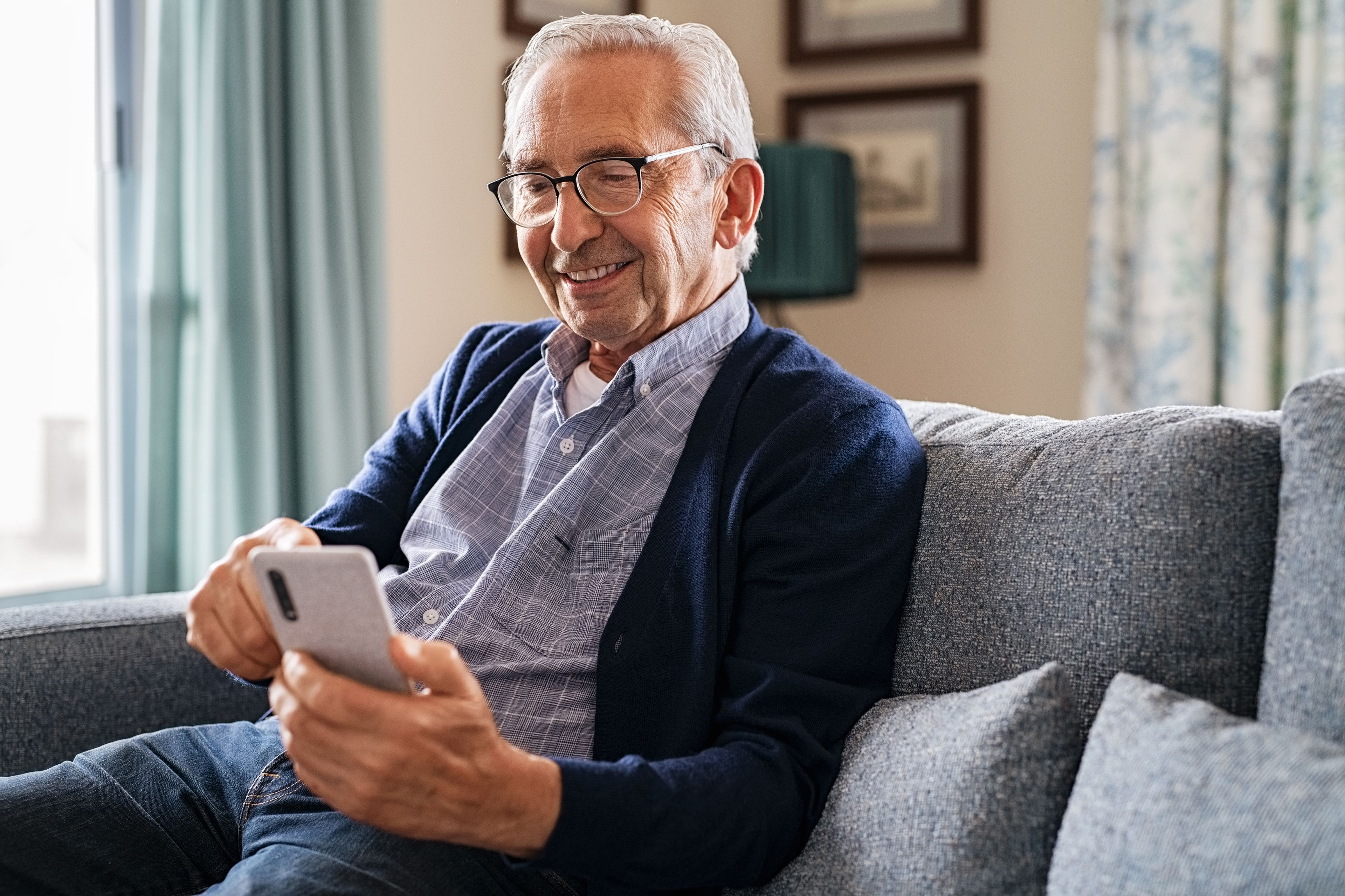 Smiling older person sitting at home using smart phone