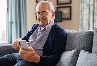 Smiling older person sitting at home using smart phone