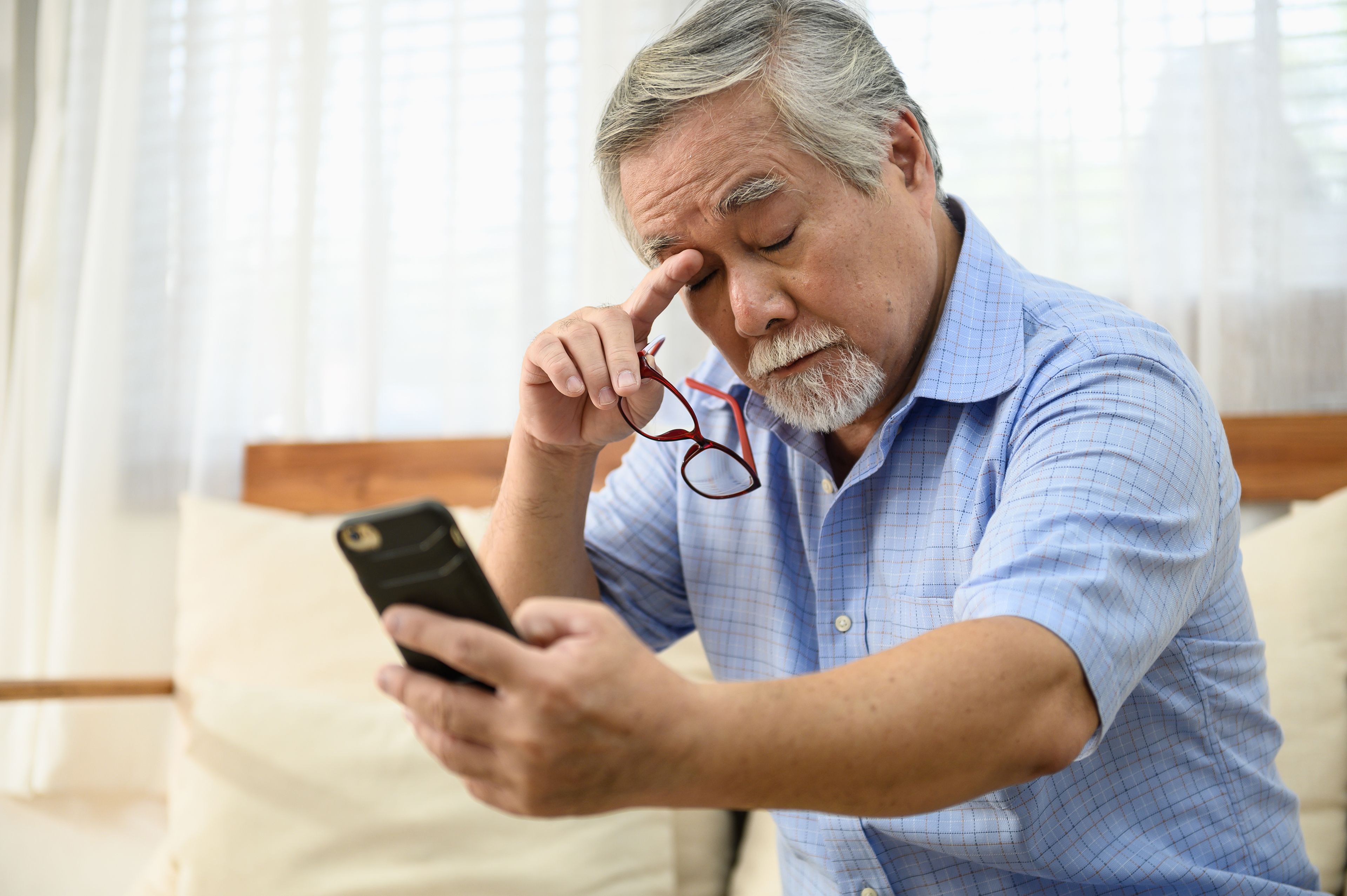 Older person rubbing eyes while looking at smart phone