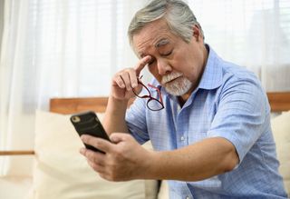 Older person rubbing eyes while looking at smart phone