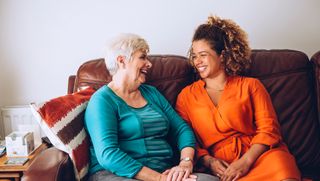 Younger carer laughing with older person on couch