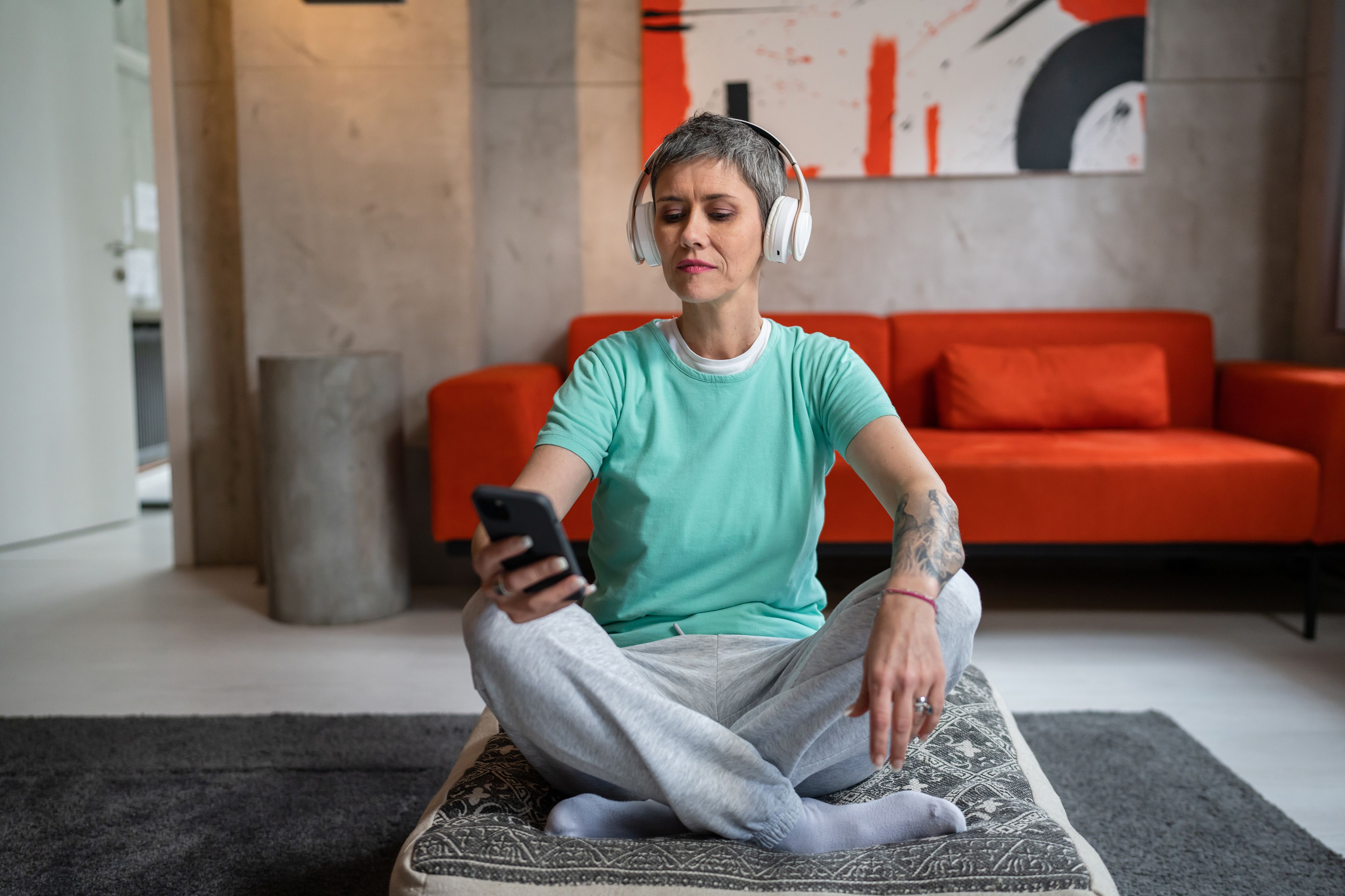 Person seated on floor at home using headphones and smart phone to meditate