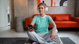 Person seated on floor at home using headphones and smart phone to meditate