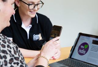 An Assistive Technology specialist works with a Client using their smartphone and a laptop.