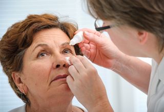 Medical professional helping apply older person's eye drops