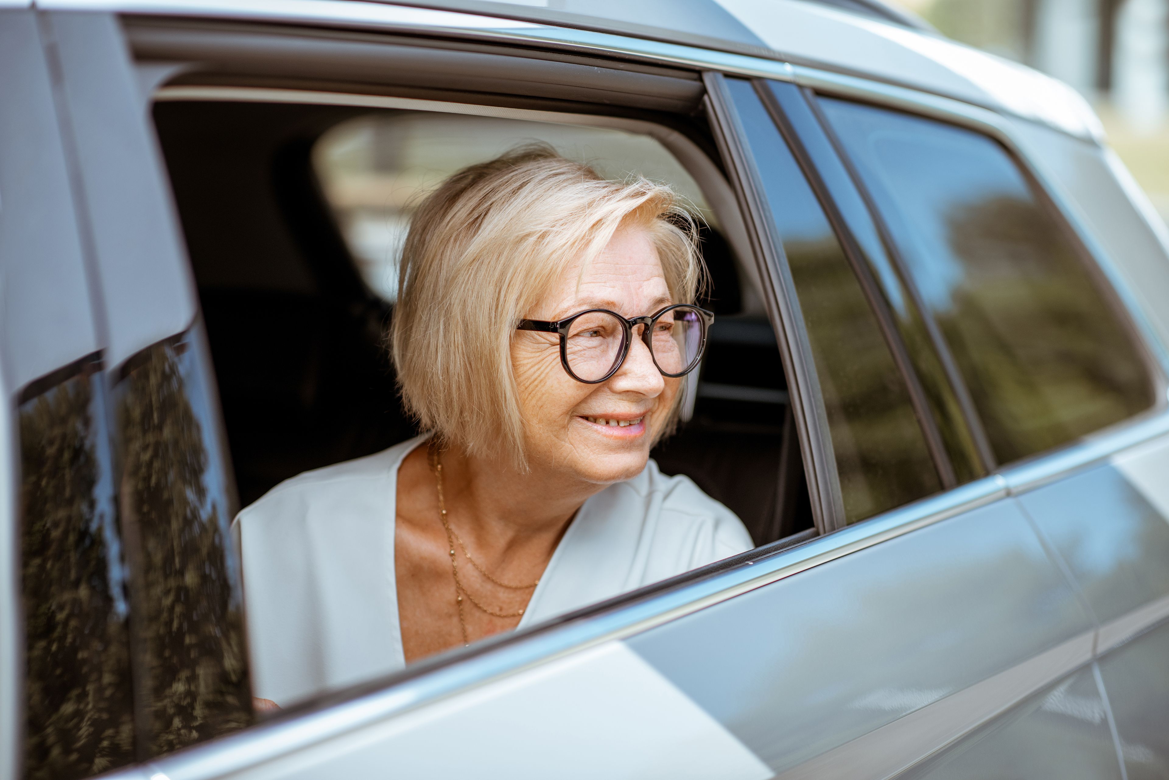 Smiling older person looking out car window from passenger seat