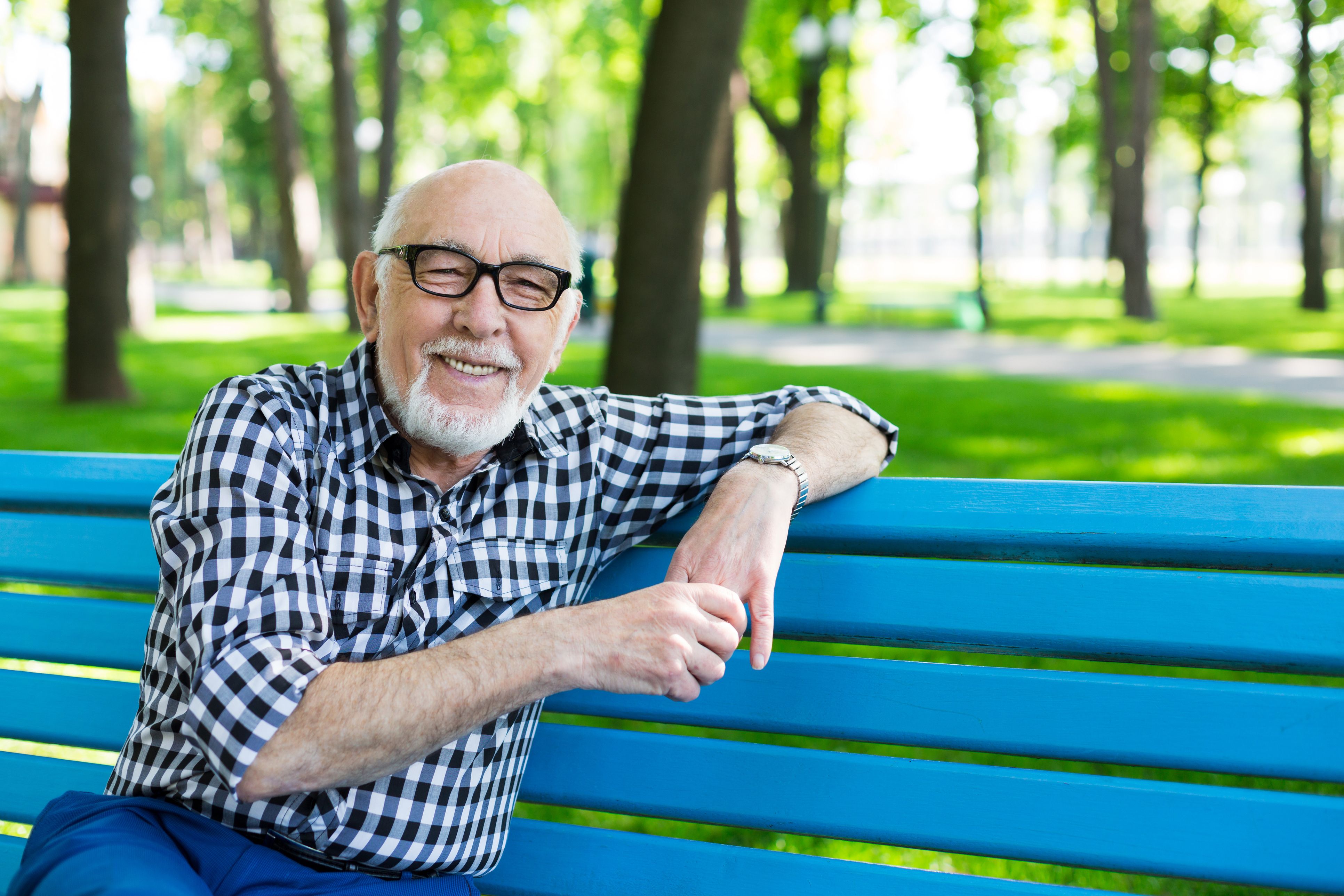 Older man in checkered shirt with glasses sitting on a park bench.