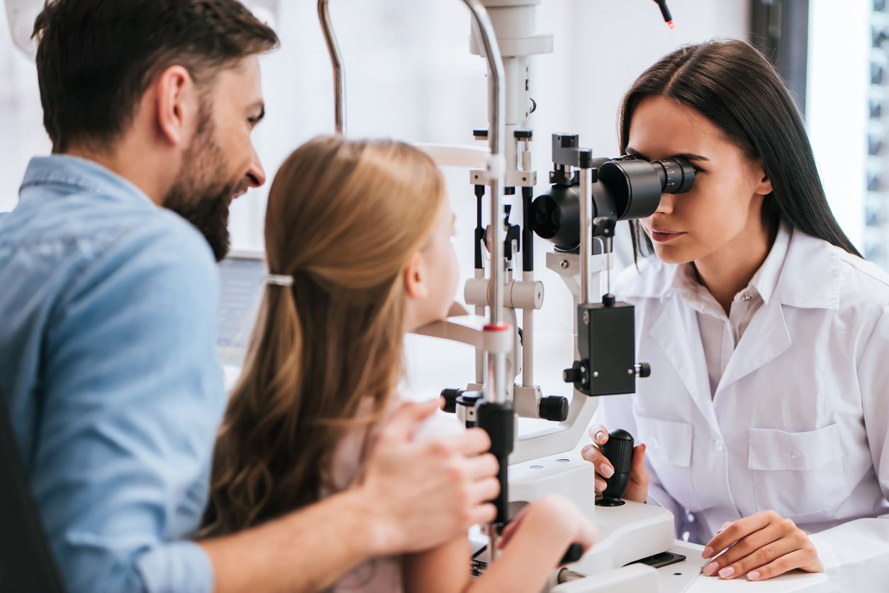 Father taking his school-aged daughter for an eye test with a medical professional