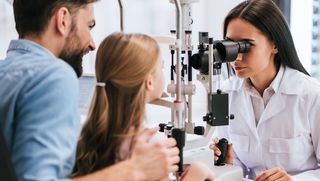 Father taking his school-aged daughter for an eye test with a medical professional