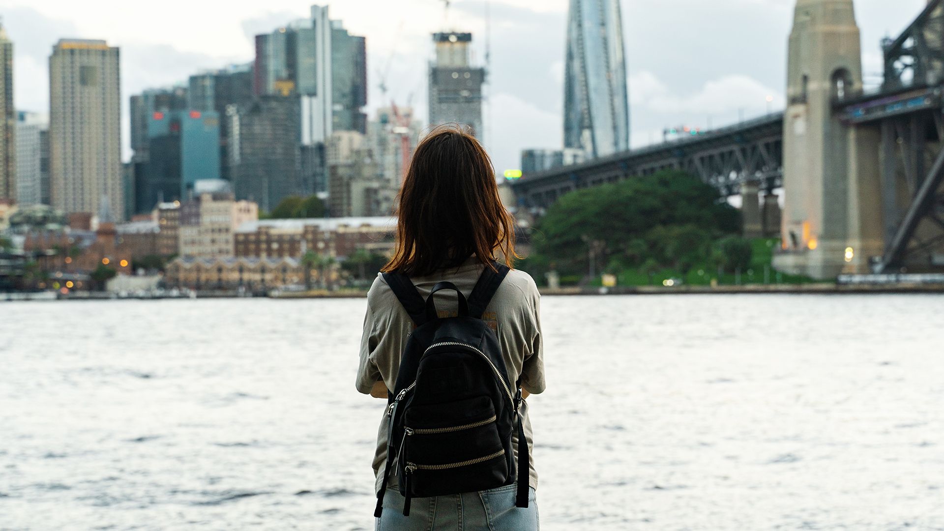 A woman standing with her back to the camera looking at Sydney Harbour