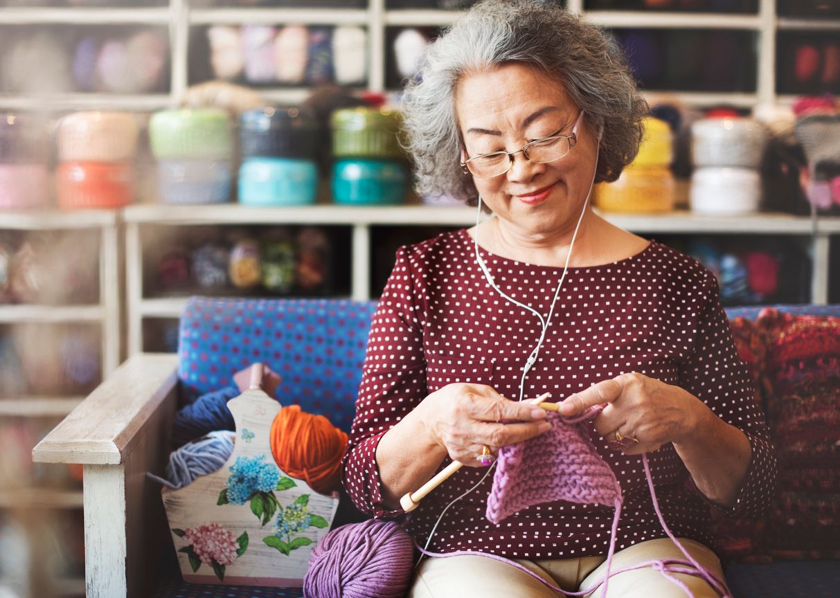 Older person knitting while listening to music using headphones