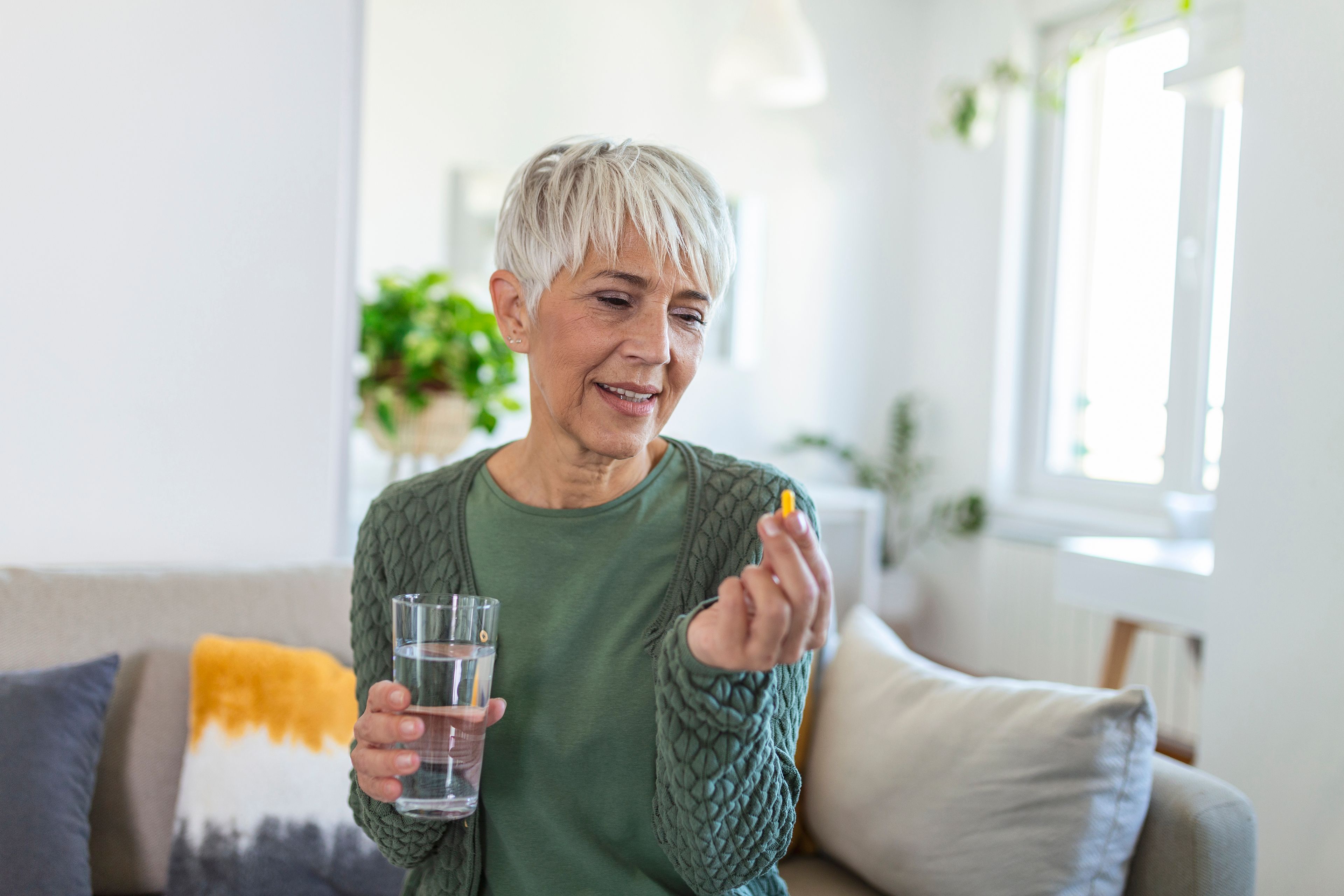 Woman looking at supplement in hand while holding glass of water