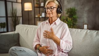 A woman sitting cross-legged on the couch with headphones in following a guided meditation
