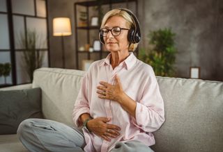A woman sitting cross-legged on the couch with headphones in following a guided meditation