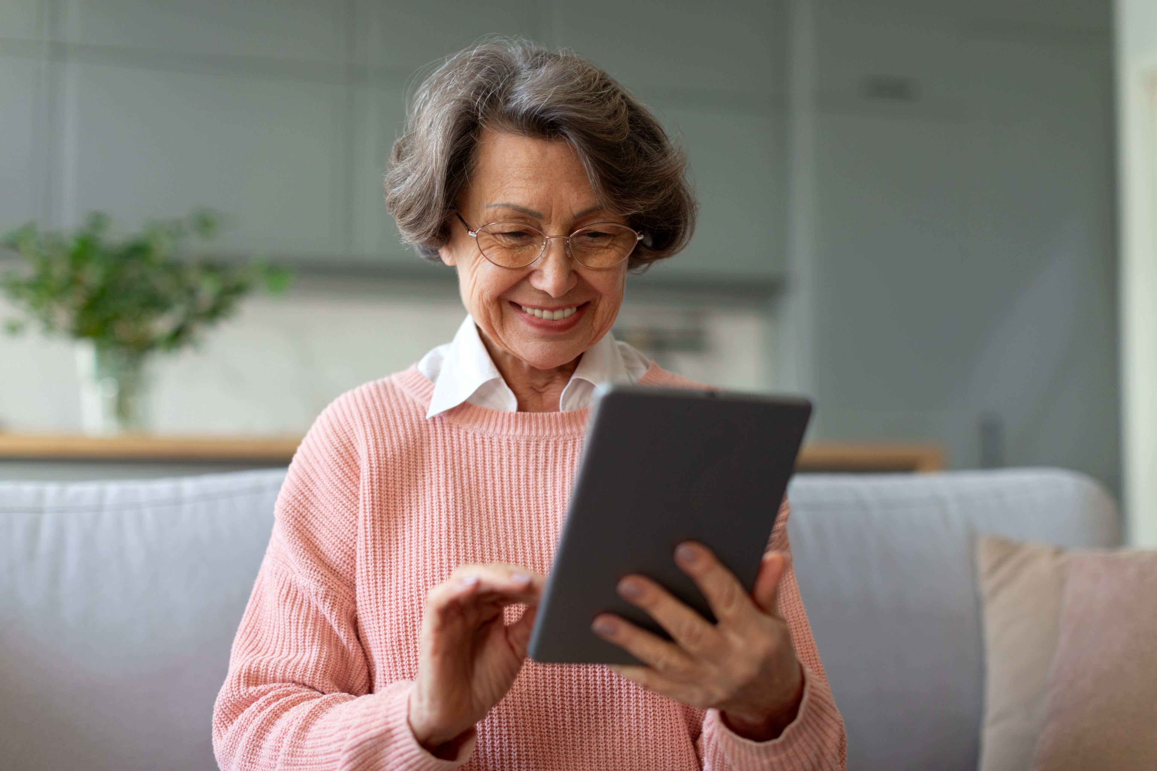 An older woman wearing glasses using a tablet and smiling