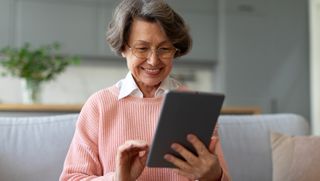 An older woman wearing glasses using a tablet and smiling
