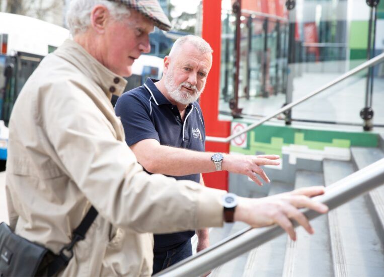 An Orientation and Mobility specialist working with a Client to navigate a set of stairs outside.