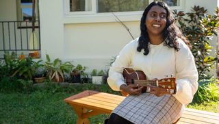 Abby playing her ukulele on a bench in her garden