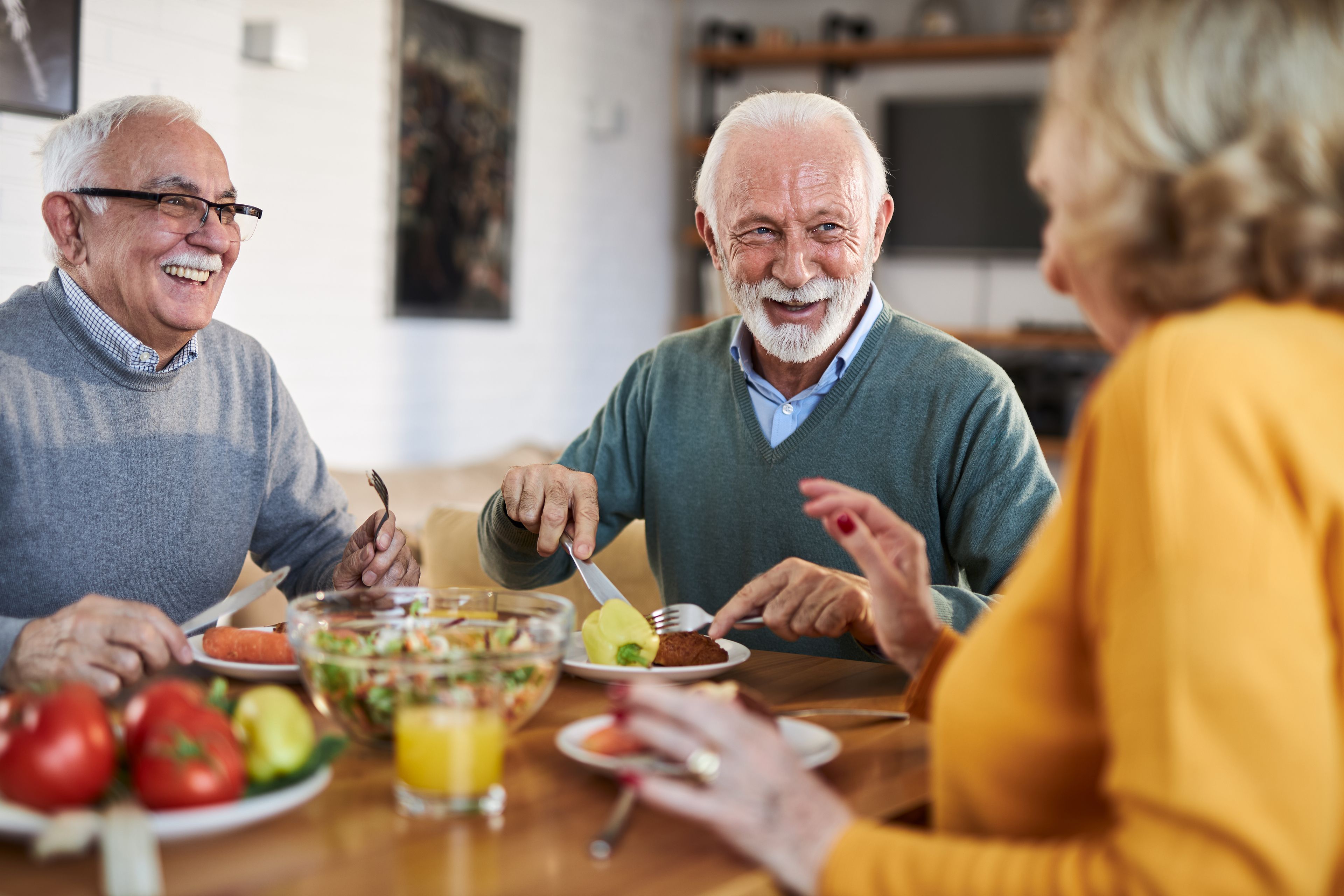 Group of older people smiling and laughing while eating at home