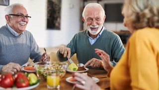 Group of older people smiling and laughing while eating at home