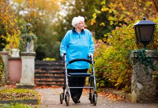 Older person walking in park using a mobility walker