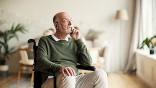 Older man in wheelchair looking pensive at home