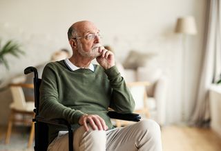 Older man in wheelchair looking pensive at home