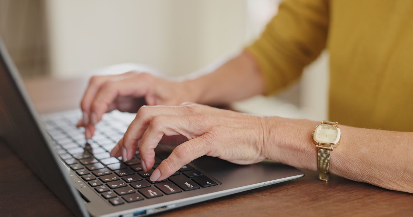 An older person's hands typing on a laptop