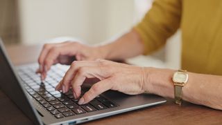 An older person's hands typing on a laptop