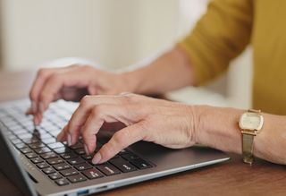 An older person's hands typing on a laptop