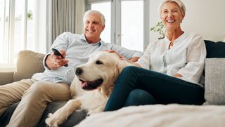 Older couple sitting on couch with dog watching television