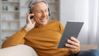 Smiling older person wearing headphones and using digital tablet