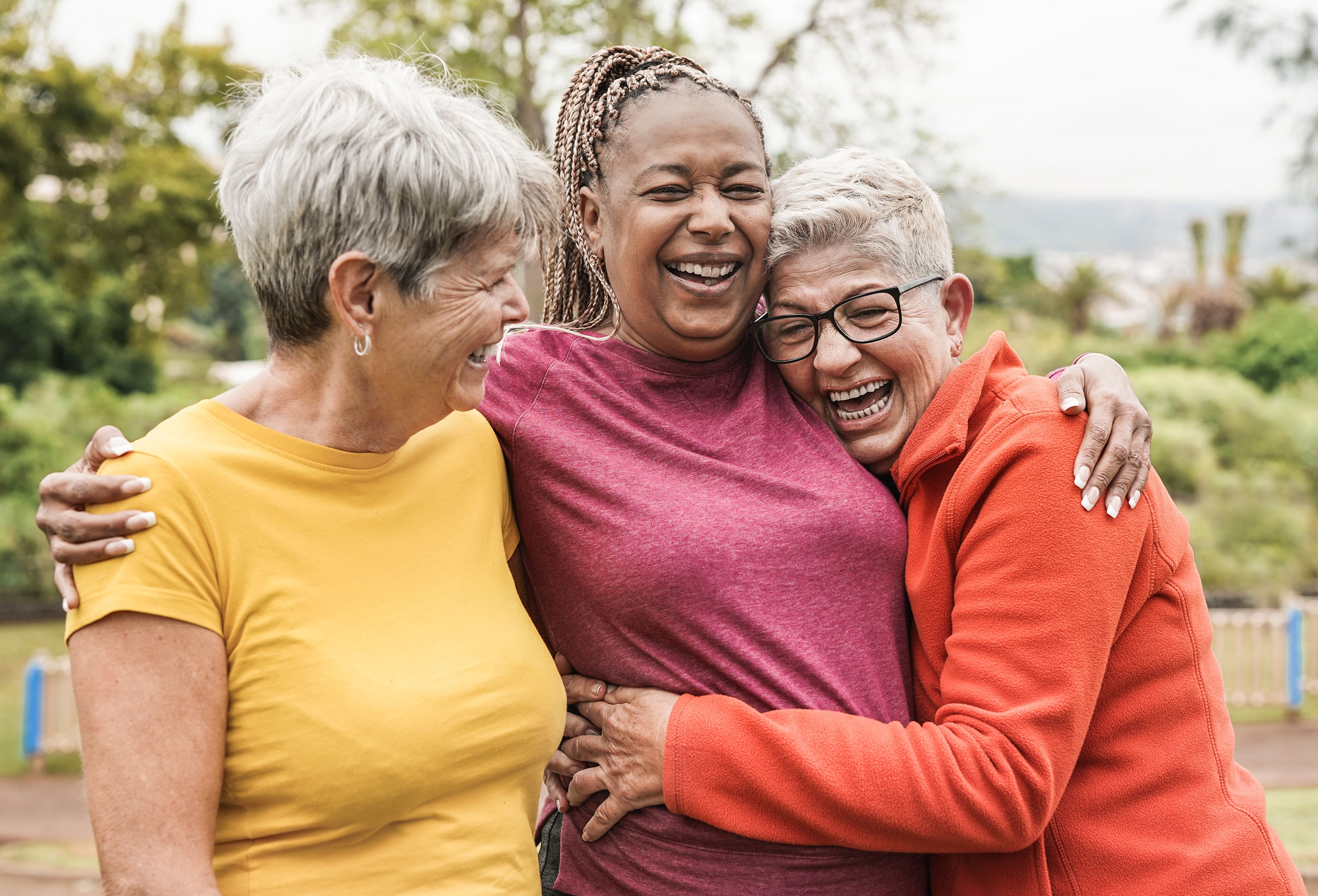 Group of three older people hugging outdoors