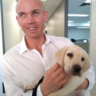 Ben Moxey smiling at the camera holding a yellow Labrador puppy.