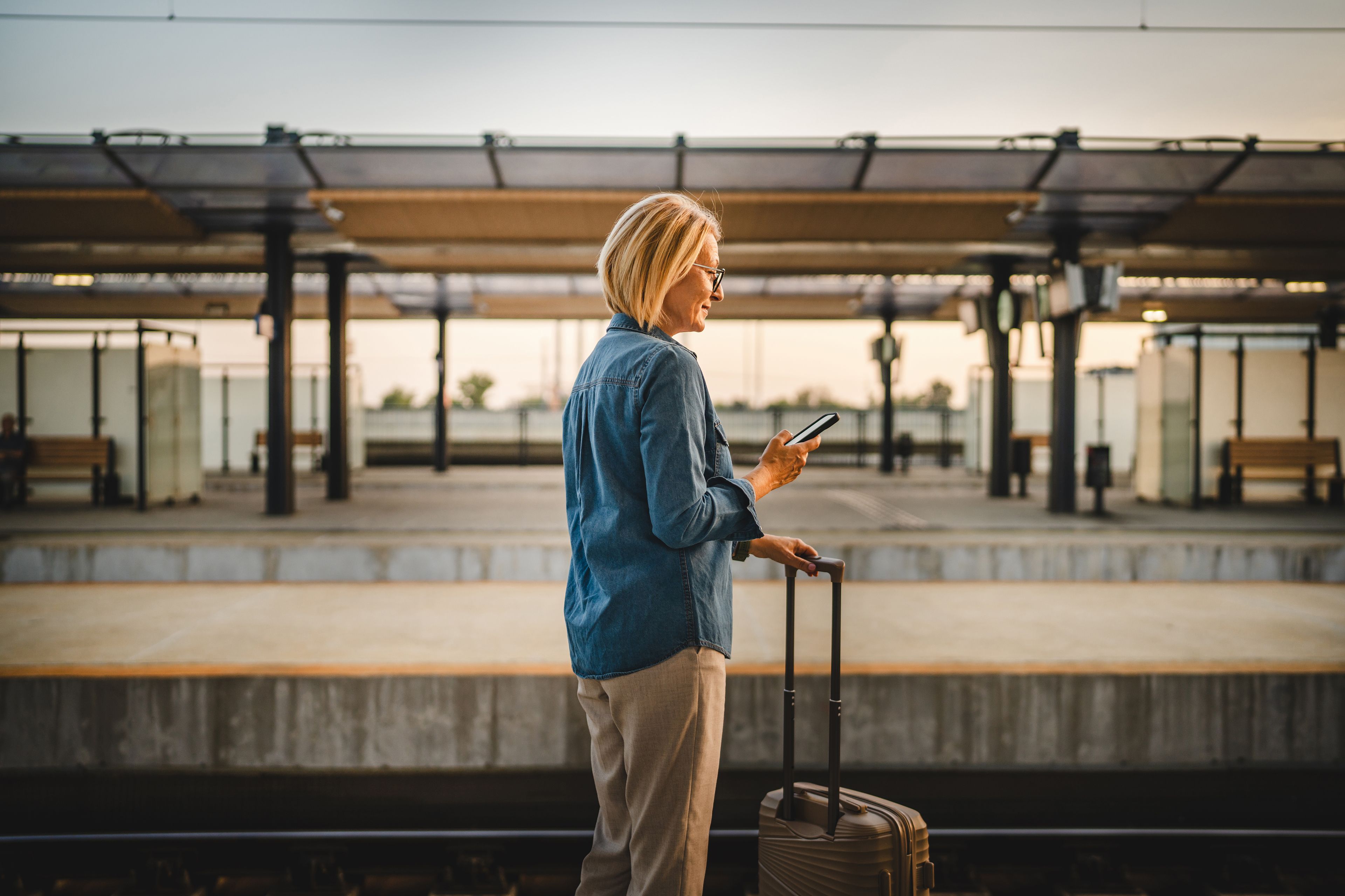 Person standing on train station platform looking at smart phone