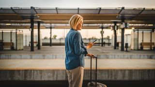 Person standing on train station platform looking at smart phone