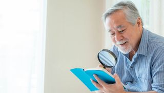 Older person using magnifying glass to read book