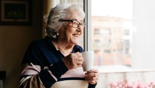Smiling older person drinking tea while looking out window